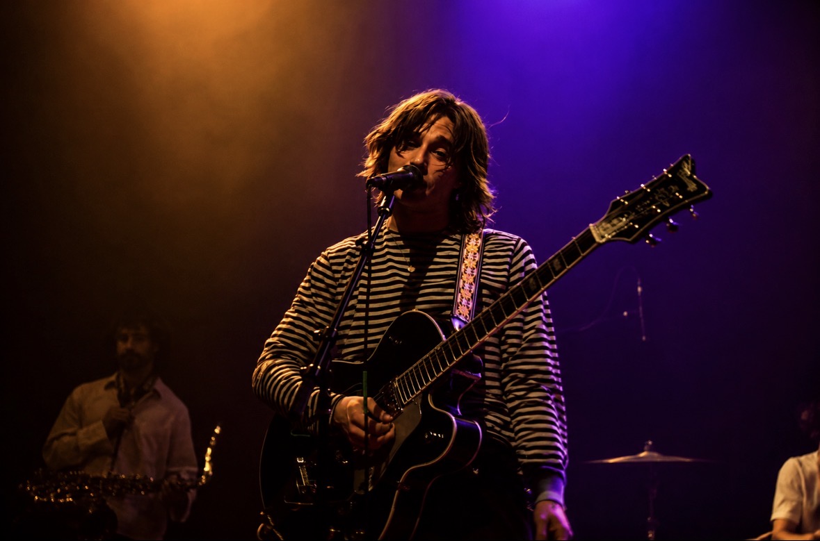 Vocalist playing guitar beneath purple and orange lights