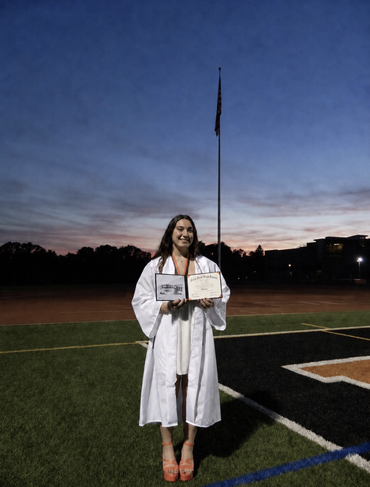 Graduate holding a diploma on a field at sunset