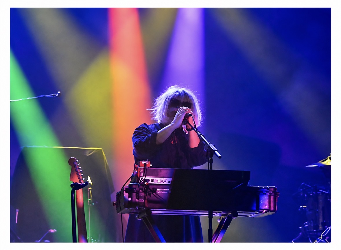 Keyboardist singing beneath green pink and purple stage beams
