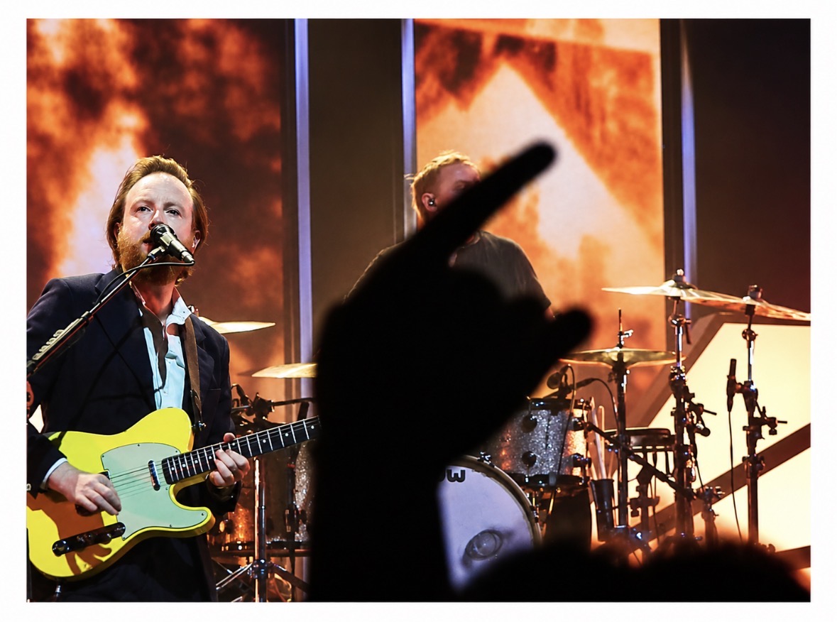 Singer with a yellow guitar and drummer behind an audience silhouette