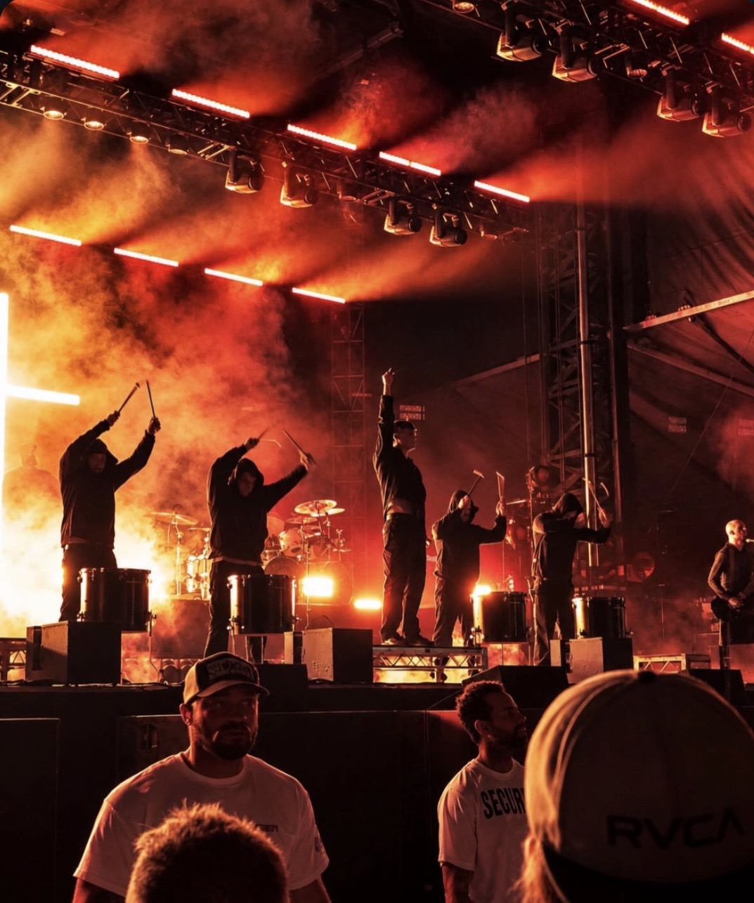 Percussionists performing under orange lights and smoke