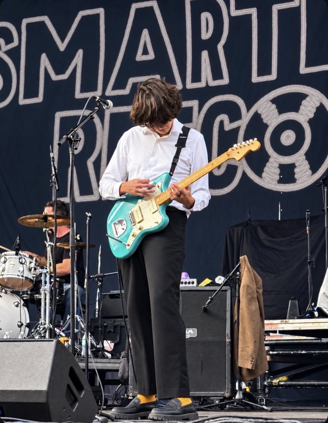Guitarist in a white shirt playing a turquoise guitar outdoors